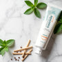 Scène zen avec un bâton de siwak naturel et un tube de dentifrice SiwakSmile sur un marbre blanc, entourés de brins de menthe fraîche, évoquant pureté et fraîcheur végétale.