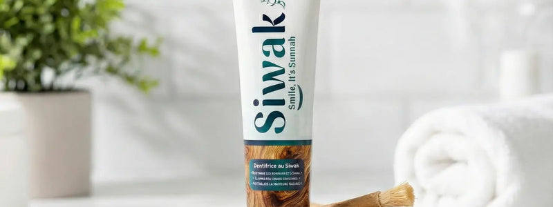 Tube de dentifrice naturel SiwakSmile et bâtons de miswak traditionnels disposés sur une pierre blanche à côté d'une brosse à dents en bambou et de poudre, illustrant une routine de blanchiment dentaire naturel dans une salle de bain lumineuse.