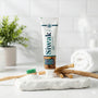 Tube de dentifrice naturel SiwakSmile et bâtons de miswak traditionnels disposés sur une pierre blanche à côté d'une brosse à dents en bambou et de poudre, illustrant une routine de blanchiment dentaire naturel dans une salle de bain lumineuse.