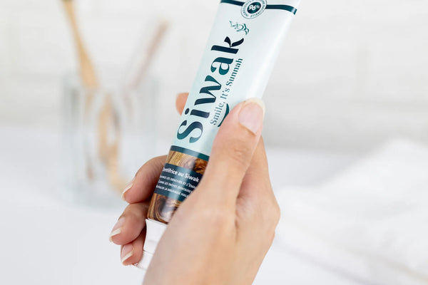 Main tenant dentifrice Siwak dans salle de bain minimaliste - Produit hygiène dentaire halal et bio