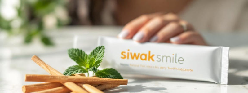 Un plateau en marbre blanc présente bâtons de siwak et dentifrice SiwakSmile entourés de feuilles de menthe et d’eucalyptus, illustrant les siwak bienfaits pour une hygiène dentaire pure et naturelle.