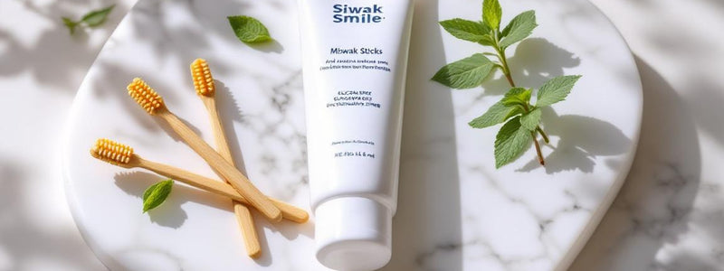 Plan détaillé de bâtons de siwak et dentifrice SiwakSmile posés sur un marbre blanc, décorés de feuilles de menthe et d’eucalyptus pour évoquer pureté et fraîcheur naturelle.