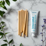 Mise en scène zen de bâtons de siwak et dentifrice SiwakSmile sur marbre blanc entourés de menthe et feuillages, illustrant comment utiliser le siwak pour une hygiène dentaire fraîche.