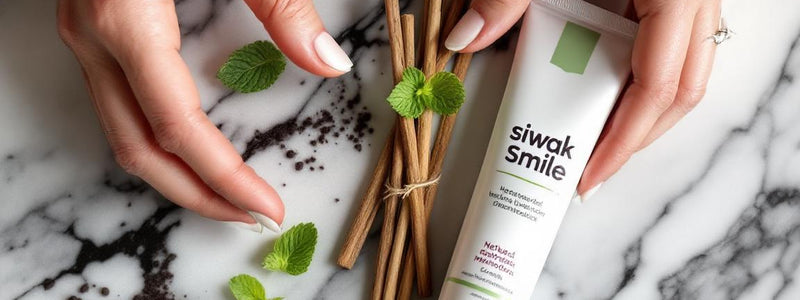 Un bâton de siwak naturel (siwak baton) posé à côté d'un tube de dentifrice SiwakSmile sur marbre blanc, entouré de feuilles de menthe fraîche, éclairé par un doux halo de lumière naturelle